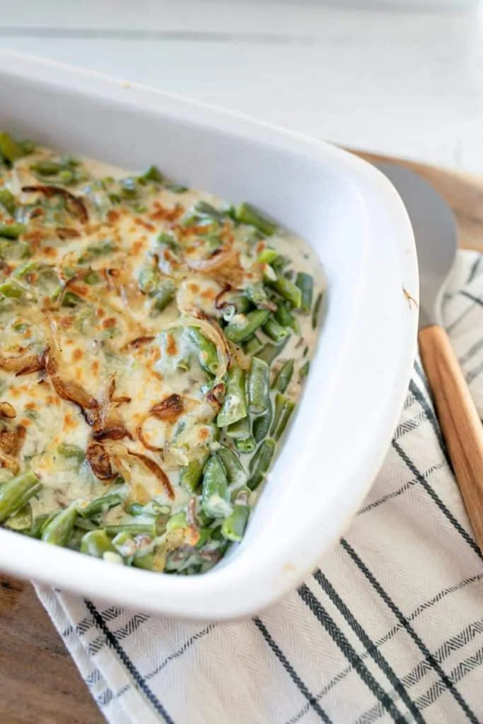 Green Bean Casserole in a white serving dish next to a wooden handled spoon.