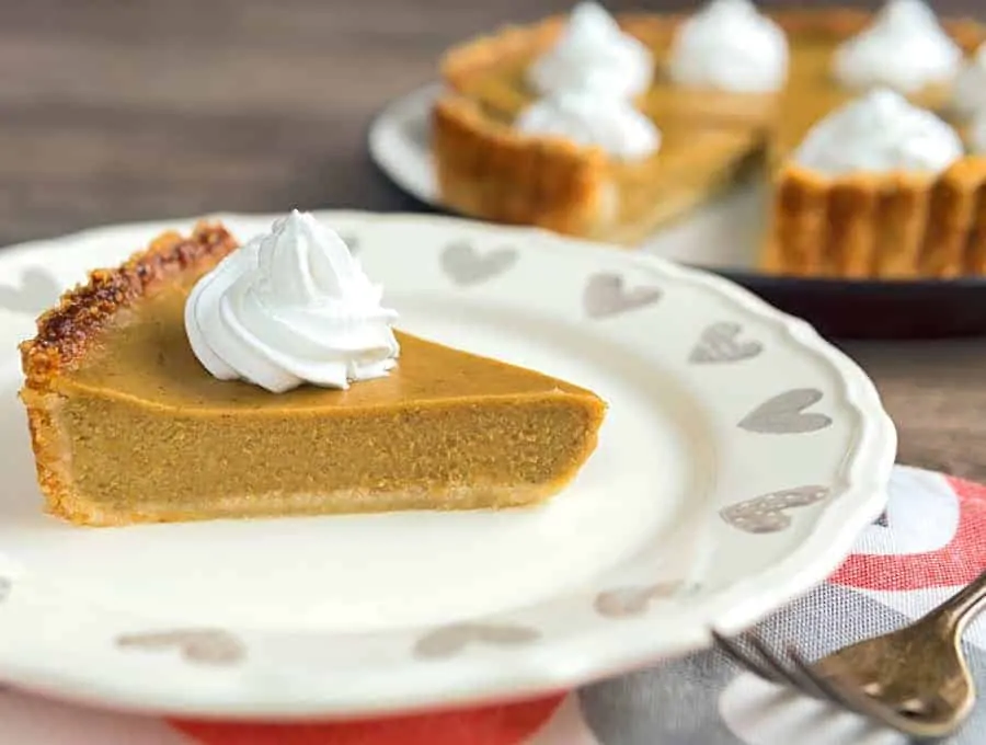 One slice of Keto Pumpkin Pie on a white plate with a dollop of whipped cream on top.