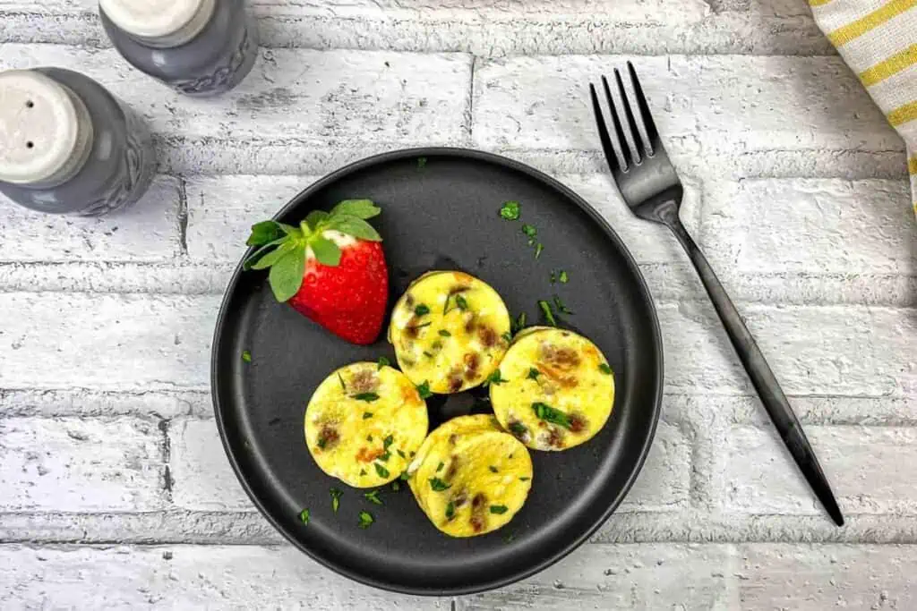Egg bites on a black plate with a strawberry on the side.