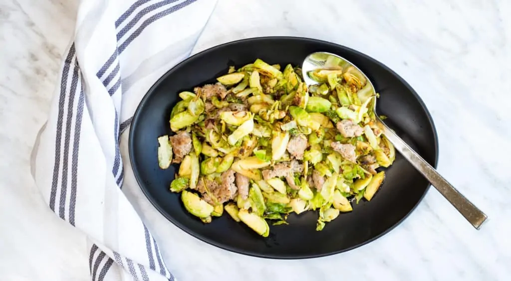 Italian brussels sprouts with sausage on a black oval bowl with a spoon