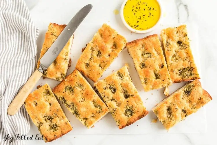 Eight Keto Garlic Bread pieces with a knife and bowl of herbed melted butter.