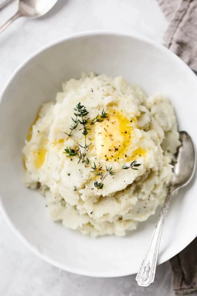 Silky Mashed Cauliflower with butter and rosemary garnish in a white bowl with a spoon.