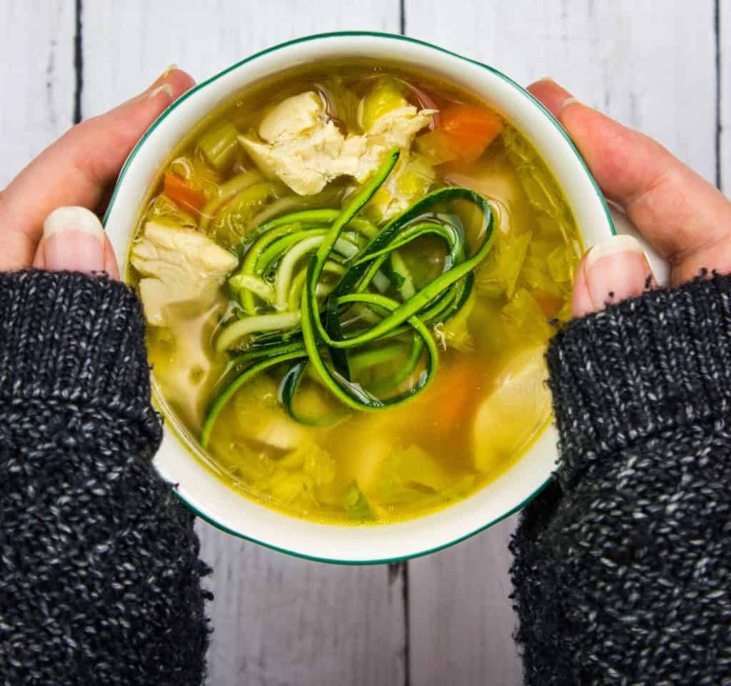 grandma's keto chicken zoodle soup in a bowl held between two hands