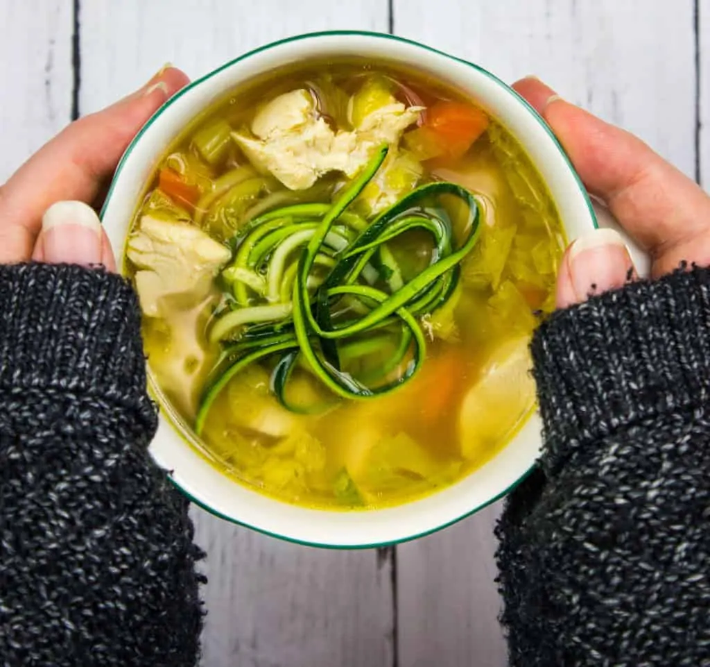 grandma's keto chicken zoodle soup in a bowl held between two hands