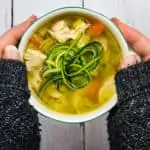 grandma's keto chicken zoodle soup in a bowl held between two hands