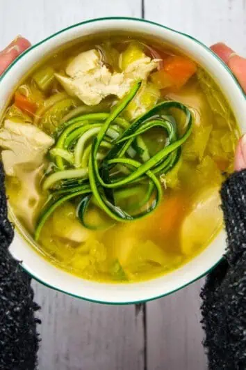 grandma's keto chicken zoodle soup in a bowl held between two hands