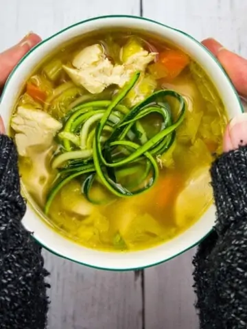 grandma's keto chicken zoodle soup in a bowl held between two hands