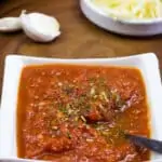 pizza sauce in a bowl with garlic and cheese in the background