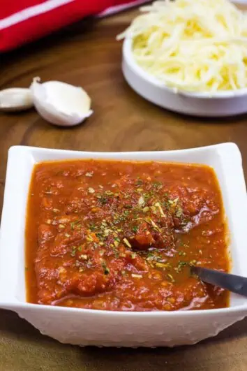 pizza sauce in a bowl with garlic and cheese in the background