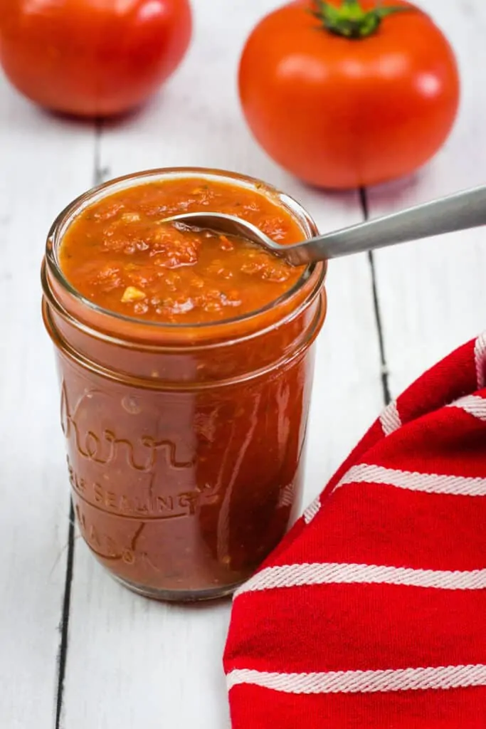 keto pizza sauce in a jar with a spoon and tomatoes in the background