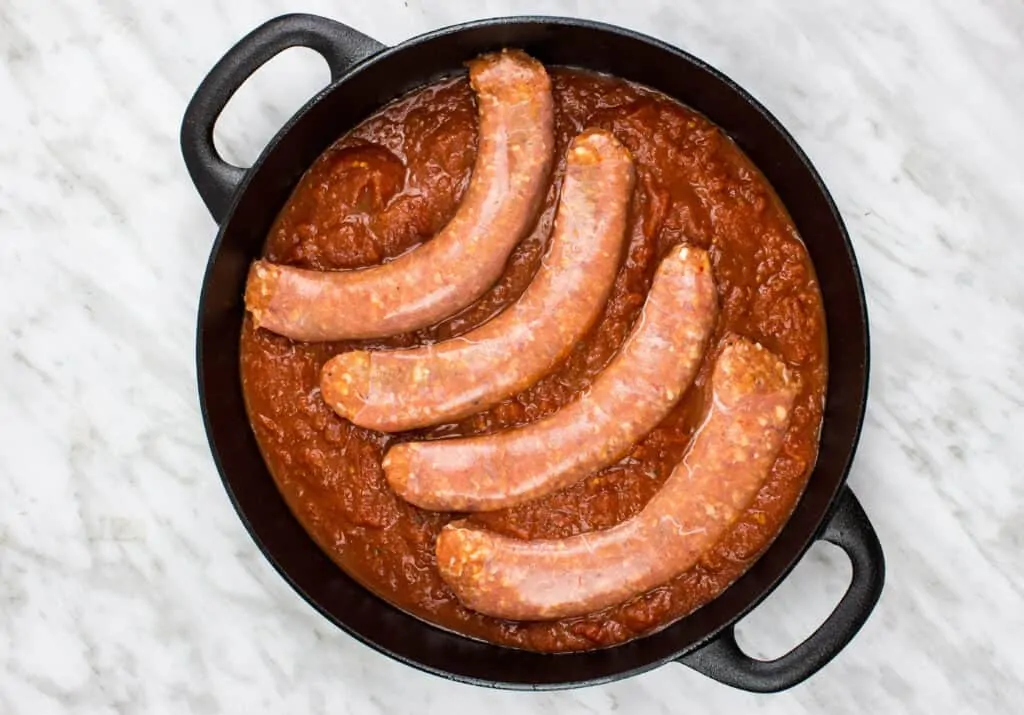 four sausage links on top of the sauce in a dish
