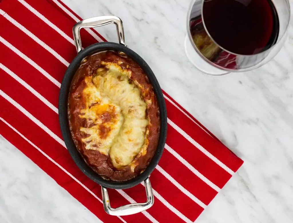 sausage parmigiana in a serving dish and a glass of wine