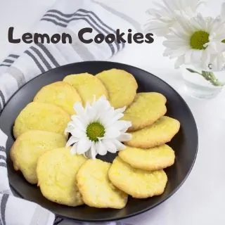 A circle of lemon cookies on a black plate surrounding a small white daisy in the center.