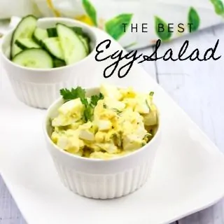 the best egg salad in a ramekin with cucumber slices in the background