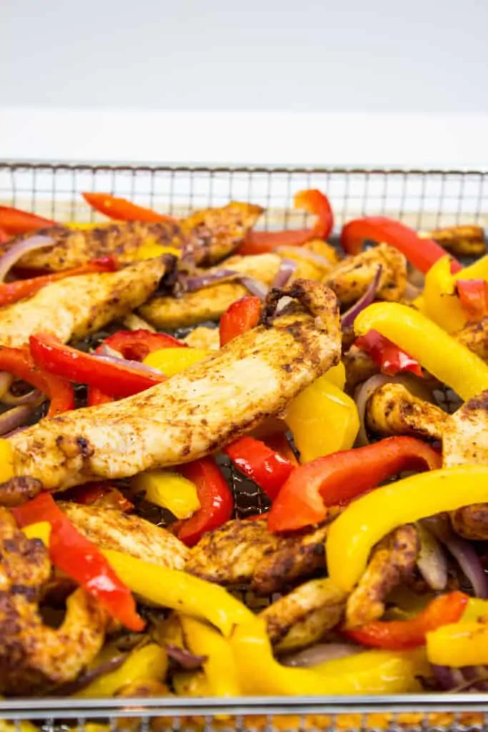 air fryer chicken with peppers and onions in the air fryer basket ready to eat