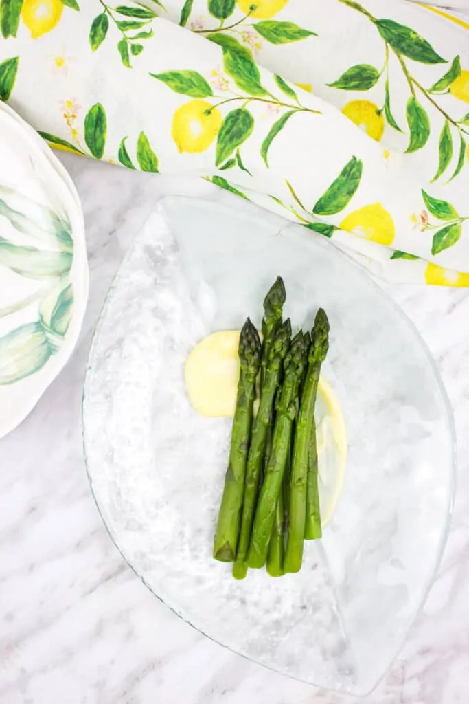 keto asparagus with lemon sauce on a plate with napkin and plates in the background