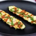 two zucchini pizza boats on a black palte