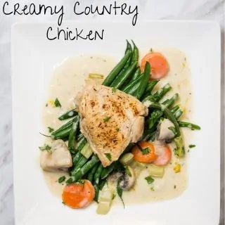 A baked chicken breast covered with a cream and vegetable sauce resting on a bed of cooked green beans.