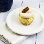 keto pecan cupcake with brown butter cream cheese icing on a plate, coffee cup in background