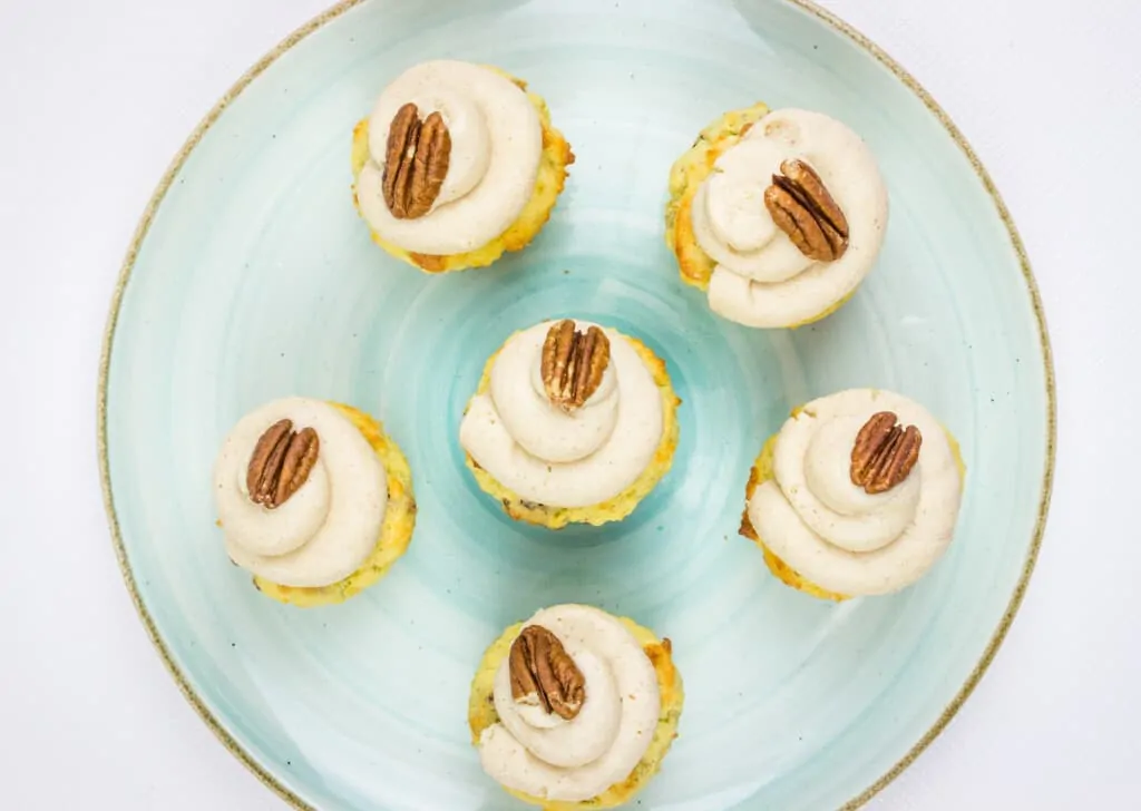 six keto pecan cupcakes with brown butter cream cheese icing on a light green plate