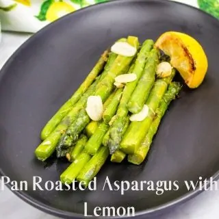 keto pan-roasted asparagus with garlic on a black plate with lemon