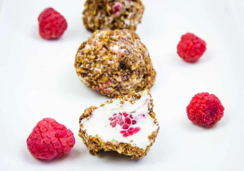 frozen cheesecake bites on a plate with raspberries