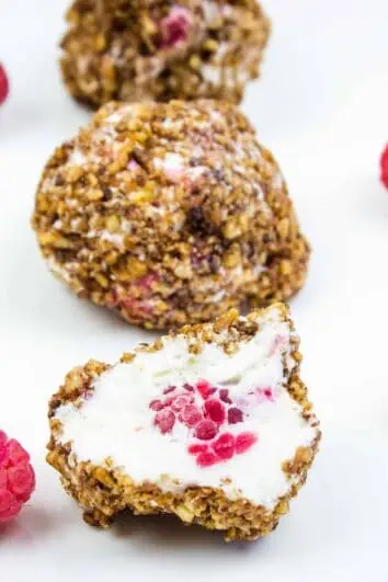 frozen cheesecake bites on a plate with raspberries