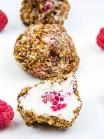 frozen cheesecake bites on a plate with raspberries