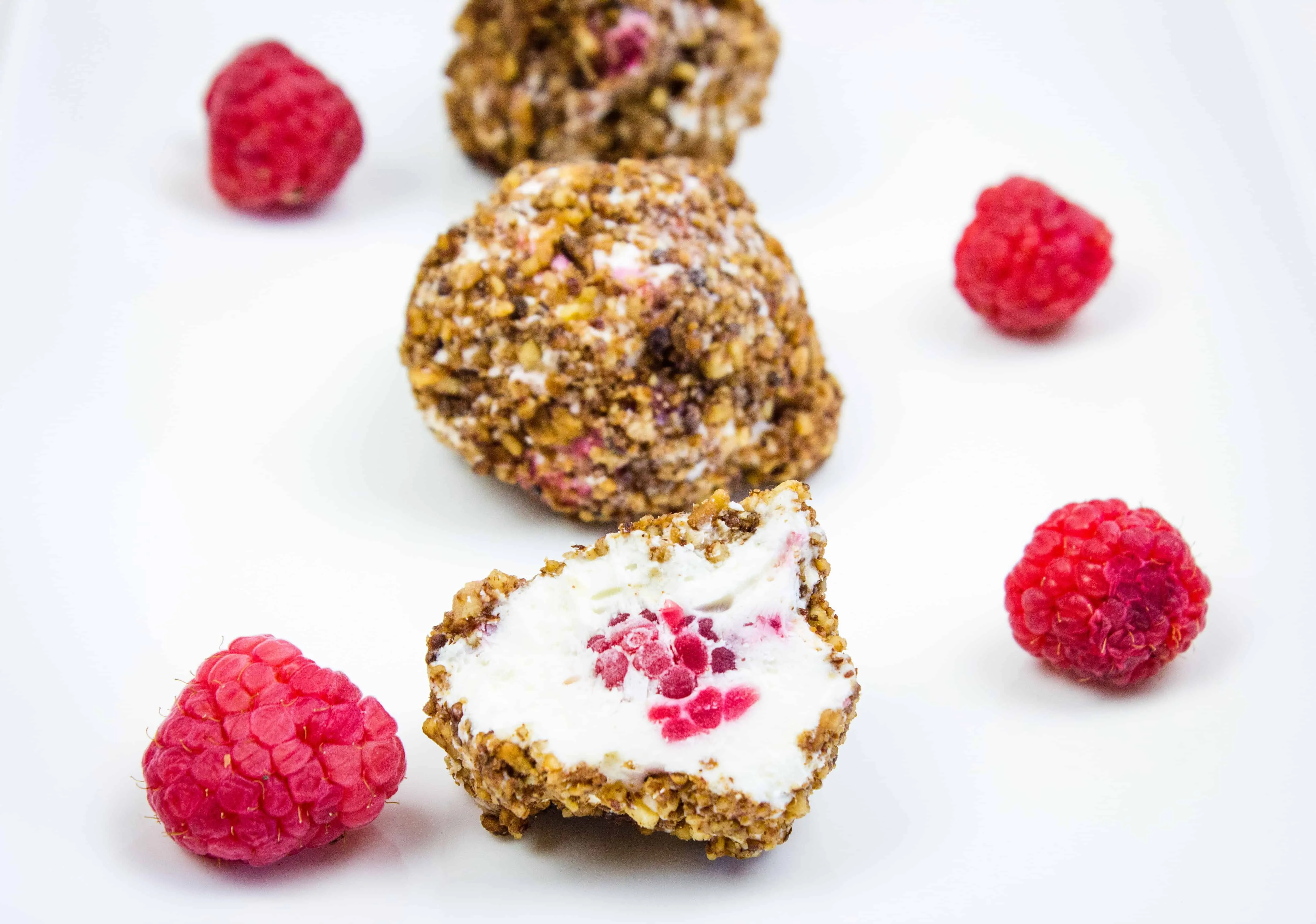 Frozen Cheesecake bites on a plate with Raspberries