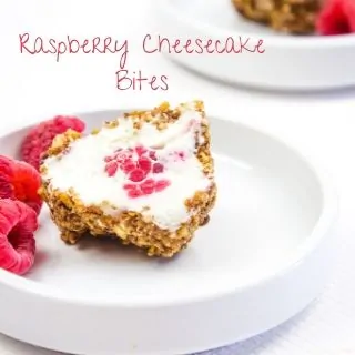 raspberry cheesecake bites on a small plate with a few raspberries nearby