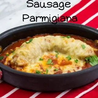 A single serving of sausage parmigiana in a black, metallic, non stick baking dish resting on a red napkin.