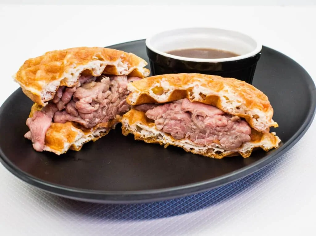 keto french dip chaffle sandwich cut in half on a black plate with a side of au jus
