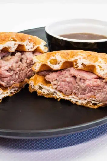 Keto French Dip Chaffwich cut in half on a black plate with a side of au jus