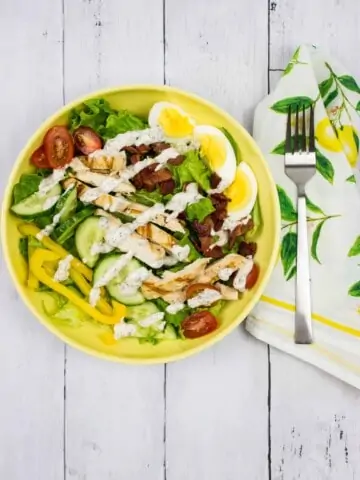 keto cobb salad with a drizzle of ranch dressing on a yellow plate