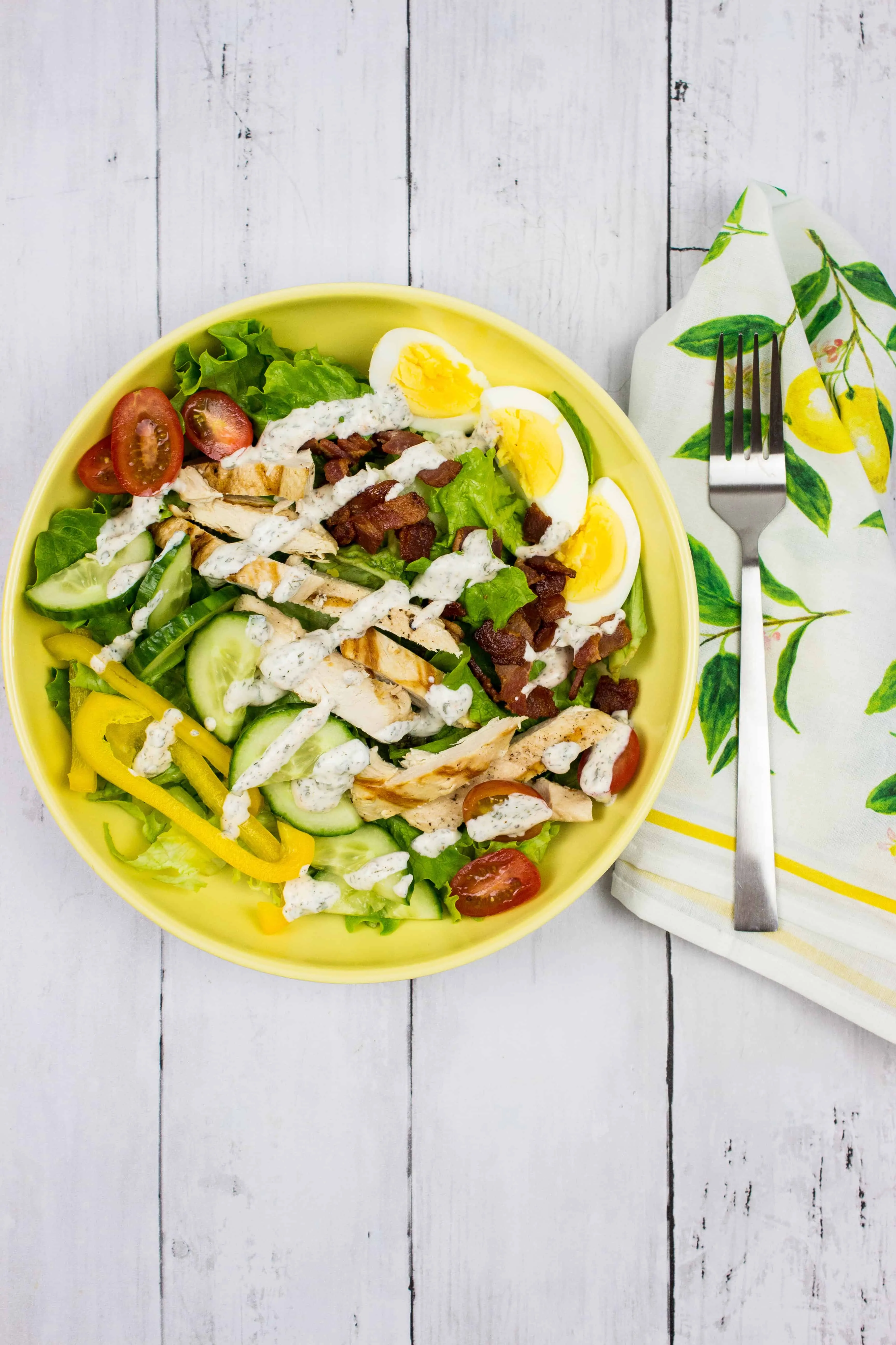 keto cobb salad with a drizzle of ranch dressing on a yellow plate