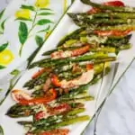 keto cheesy baked asparagus with bacon and peppers on a white serving platter