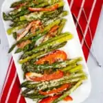 cheesy baked asparagus with bacon and peppers on a white serving platter