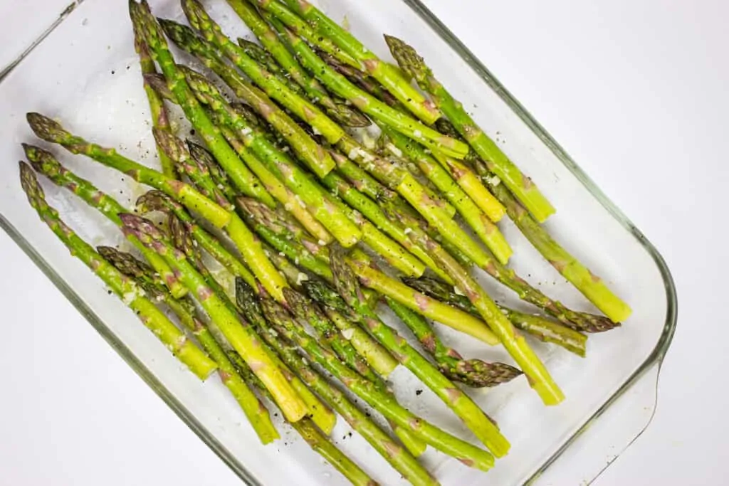 roasted asparagus in a baking dish before adding cheese and bacon