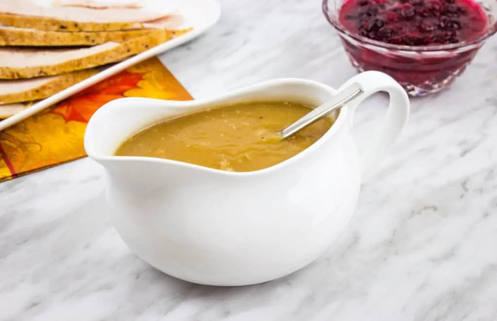 keto turkey gravy in a gravy boat with cranberry sauce and turkey in the background