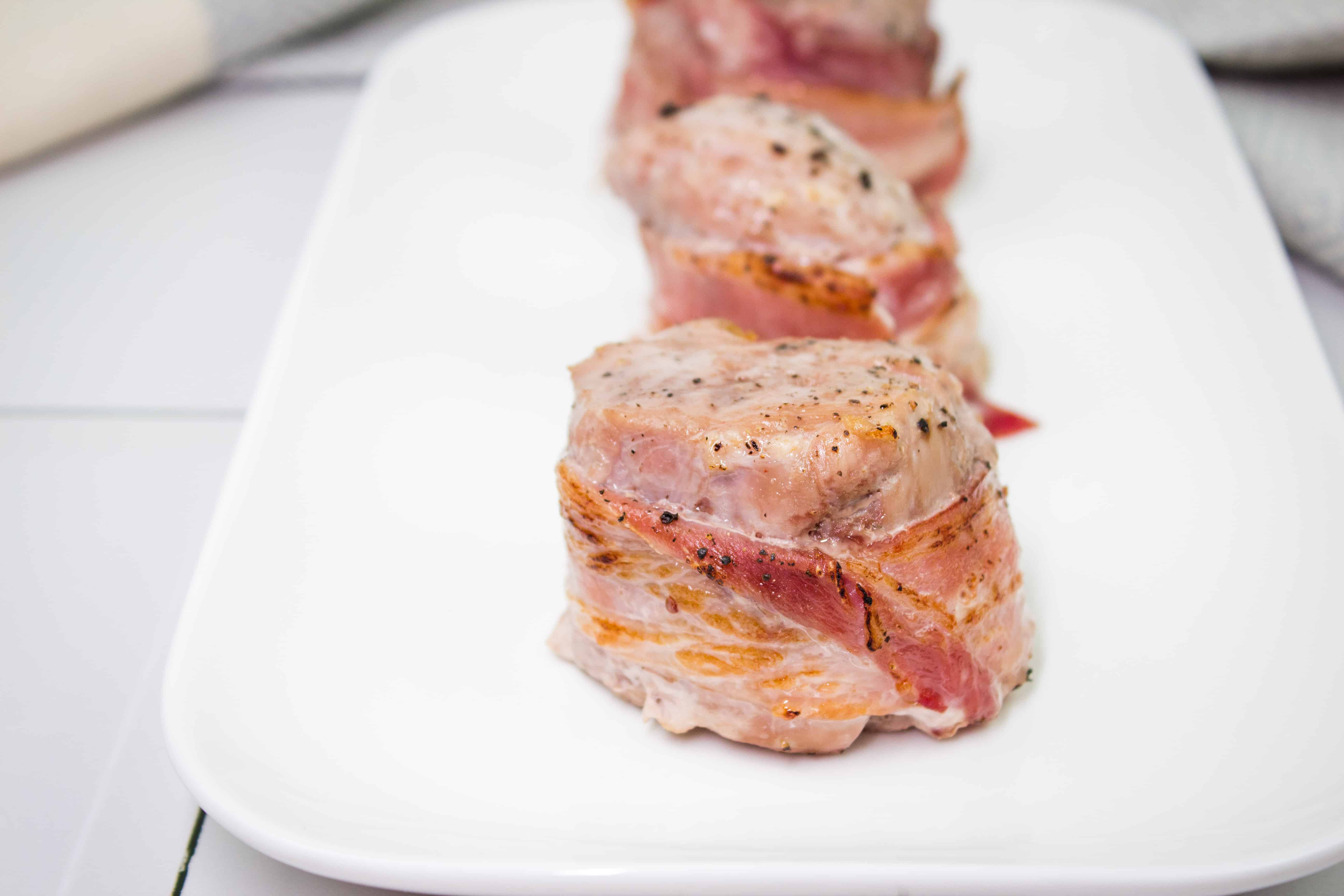 Sliced Smoked Bacon Wrapped Whole Pork Tenderloin on a white platter.