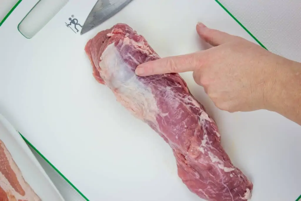 a finger pointing to the silver skin on a pork tenderloin