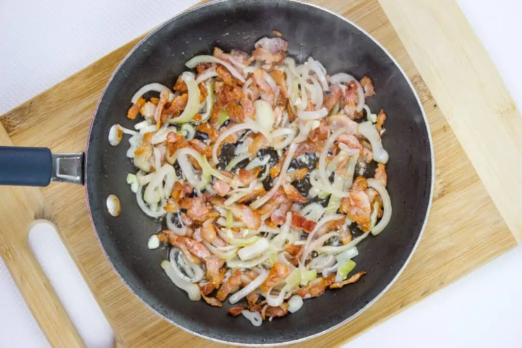 Pan fried bacon and sauteed shallots in a skillet.