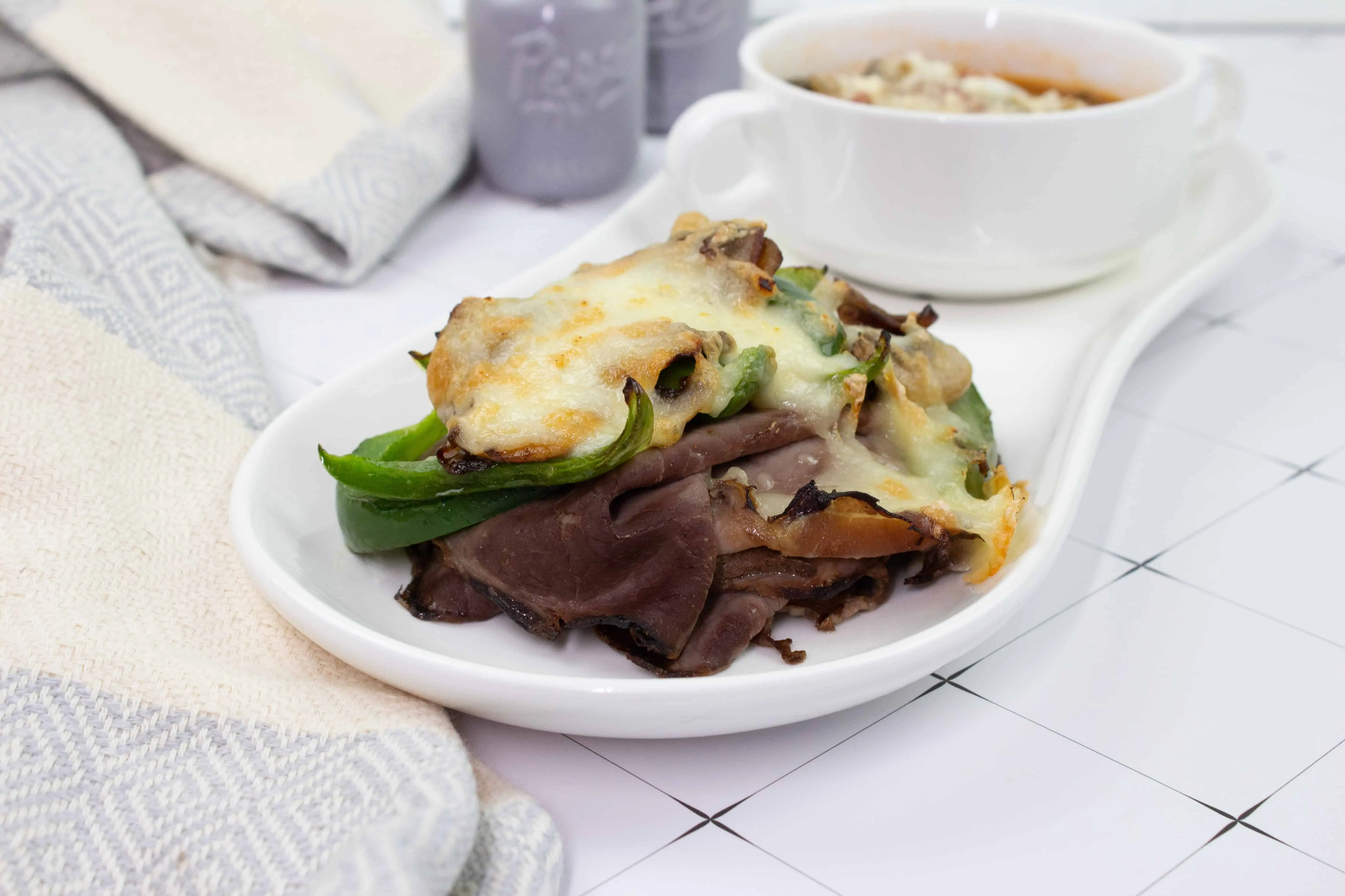 keto philly cheesesteak stacks on a plate with soup in the background