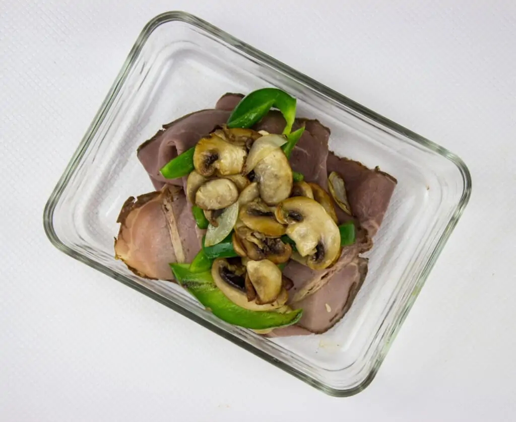 sauteed onions, mushrooms and peppers on top of sliced beef in a baking dish