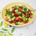 cucumber, tomato, avocado salad in a serving bowl with a napkin and spoon