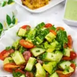 cucumber, tomato, avocado salad with chicken in teh background