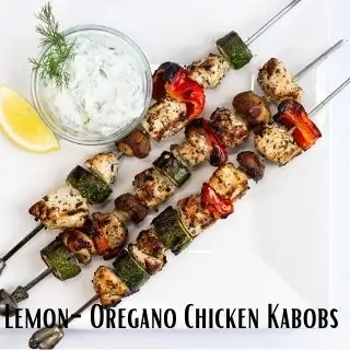 lemon oregano chicken skewers on a white plate with a side of tzatziki