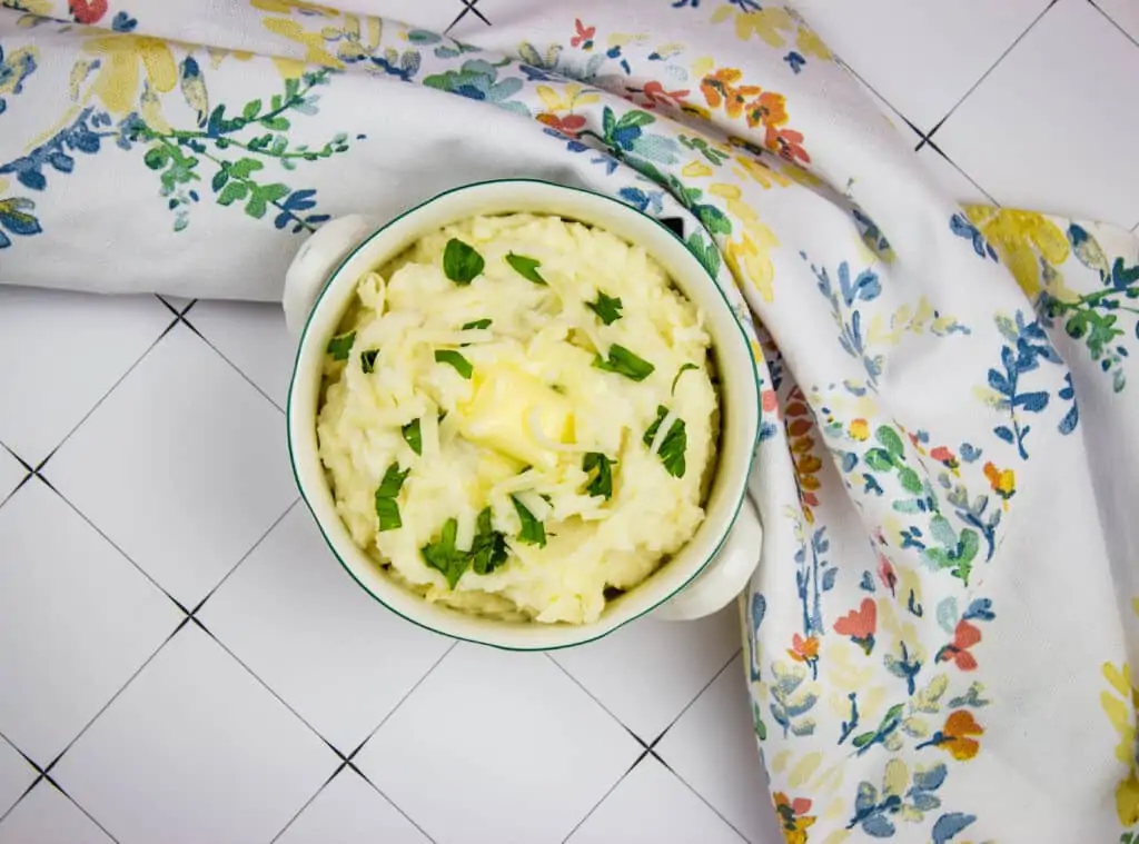 cheesy mashed cauliflower in a serving dish with a floral napkin nearby