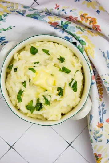 cheesy mashed cauliflower in a serving dish with a floral napkin nearby