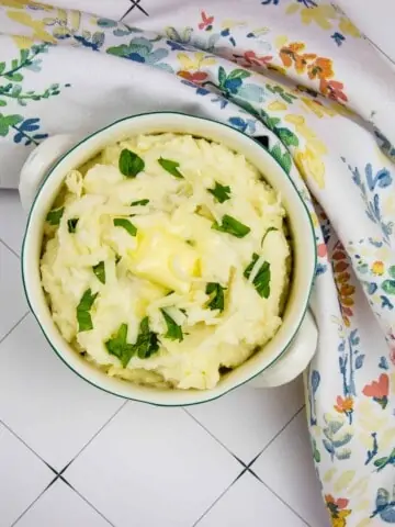 cheesy mashed cauliflower in a serving dish with a floral napkin nearby